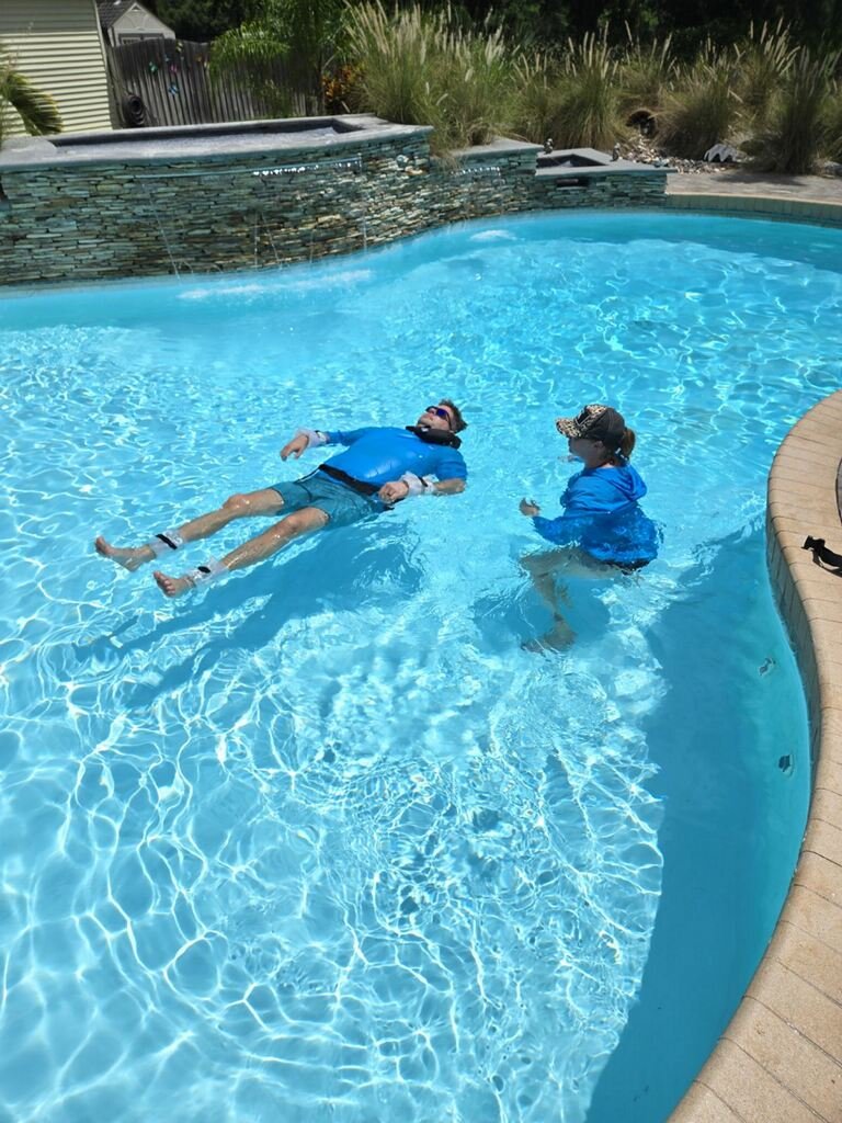 Two guests floating in a warm therapeutic pool surrounded by stone surround and lush tropical greenery